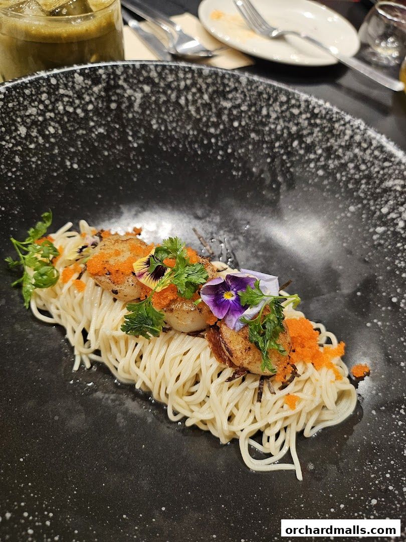 A beautifully plated dish of noodles with seared scallops and vibrant garnishes.