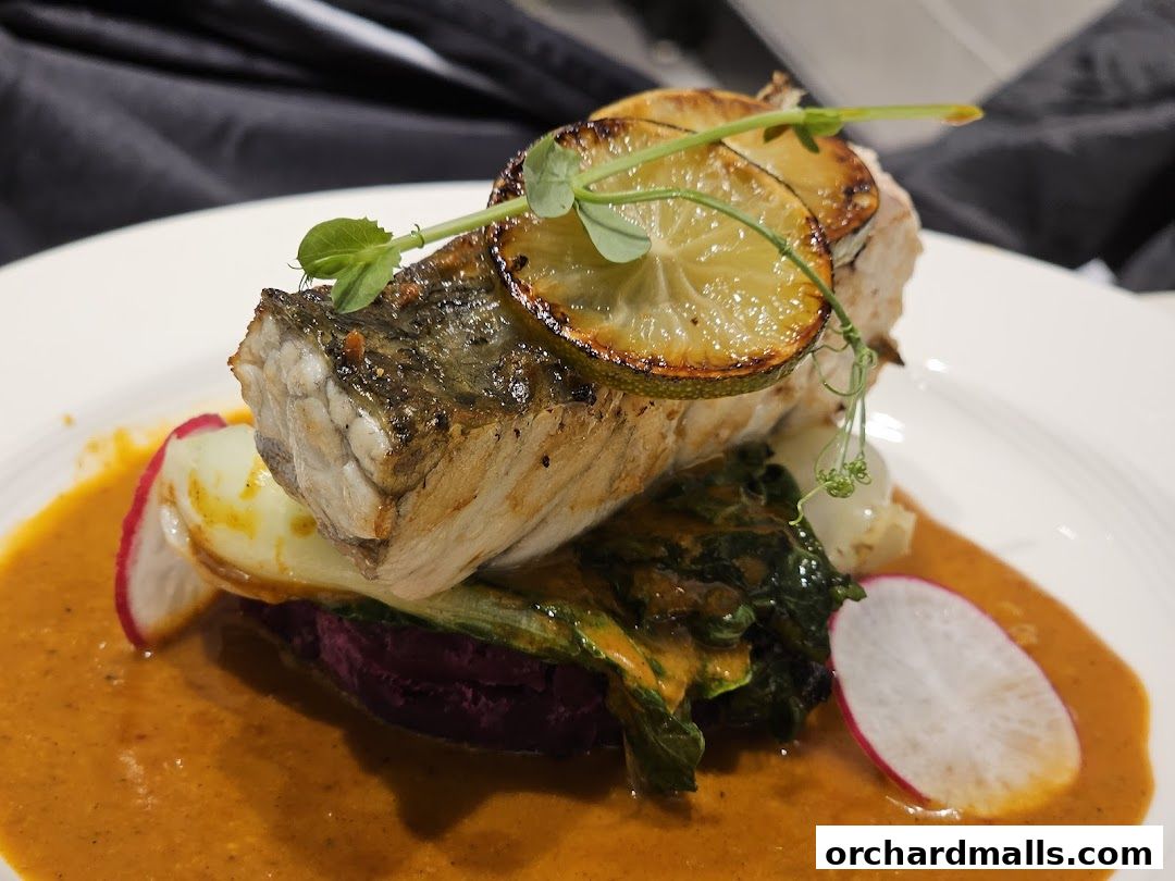 A beautifully plated dish featuring a piece of grilled fish with lime and vegetables in a rich sauce.