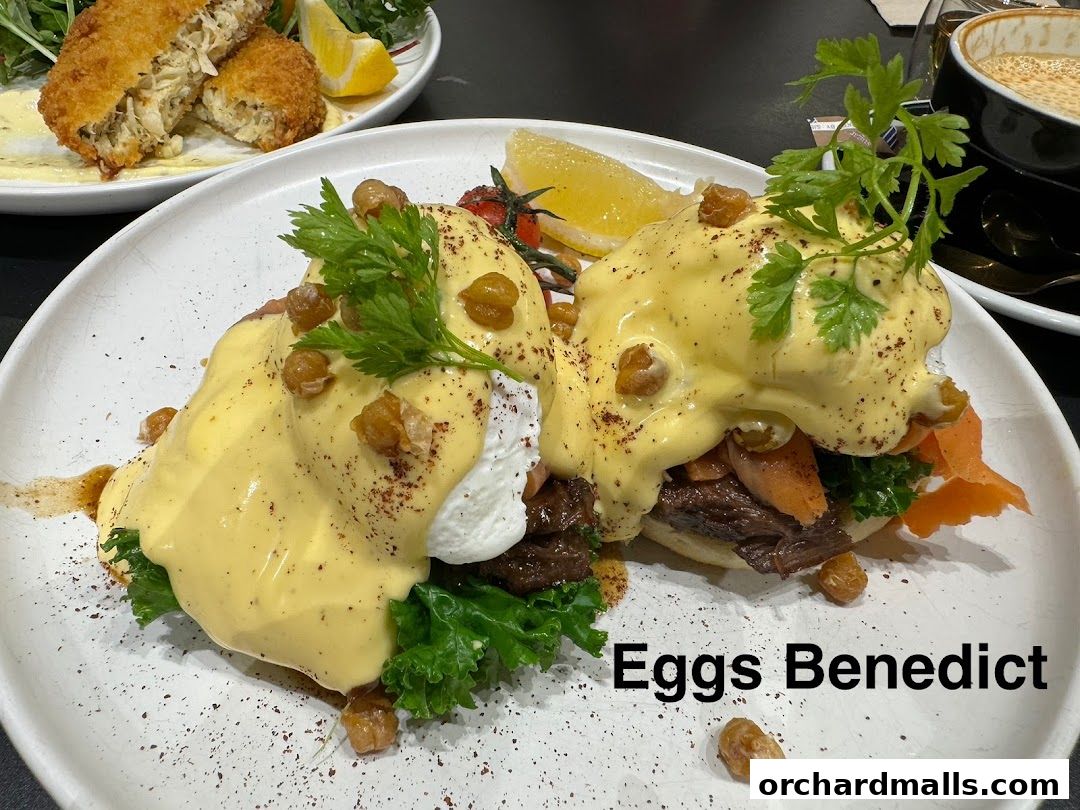 Two plates of Eggs Benedict with hollandaise sauce, garnished with parsley and served with a side of greens.