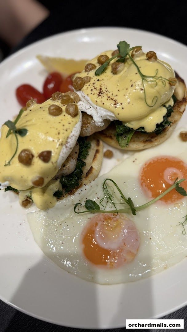 A plate of Eggs Benedict with poached eggs, hollandaise sauce, and a side of fried eggs.