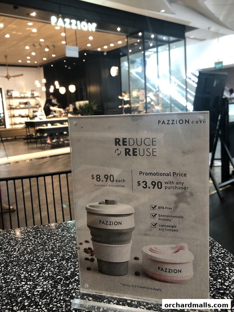 A promotional sign for Pazzion Cafe's reusable cups with a blurred shop front in the background.