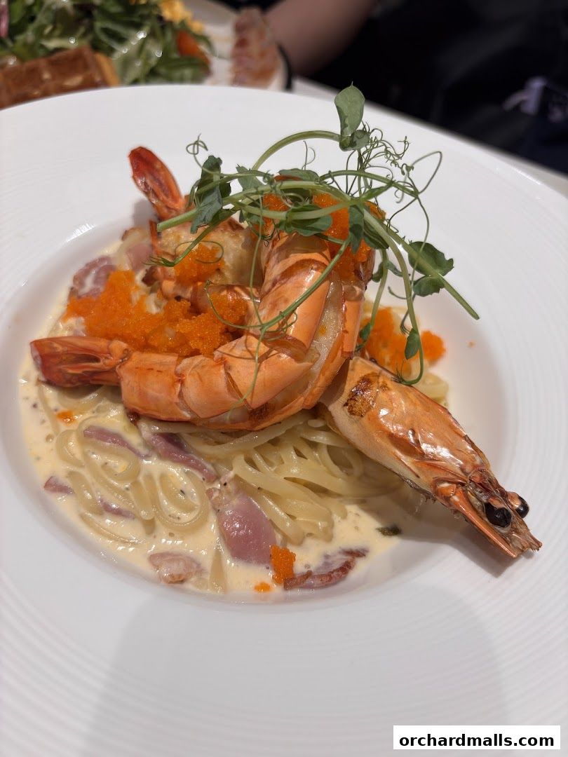 A plate of creamy pasta with large prawns and tobiko, garnished with microgreens.