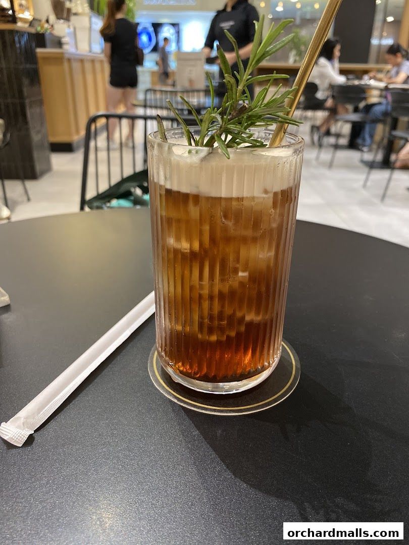 A refreshing iced tea with foam and rosemary garnish in a fluted glass.