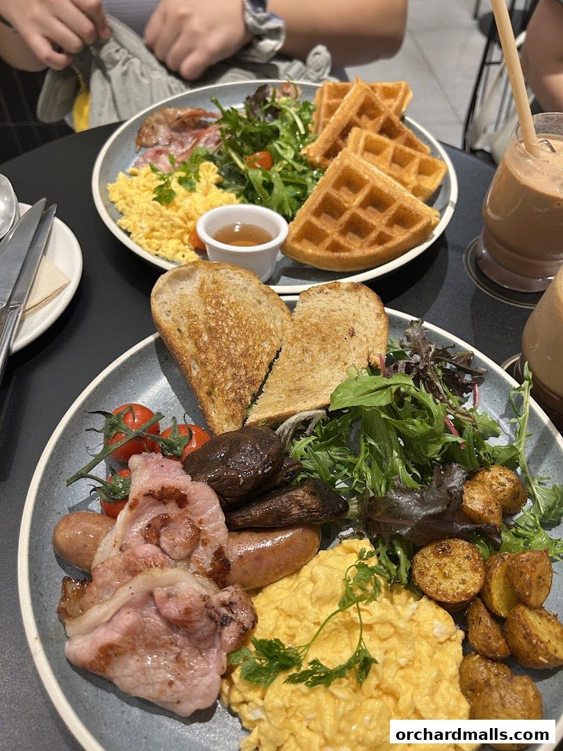 Two plates of breakfast food, including scrambled eggs, bacon, sausages, toast, and waffles.