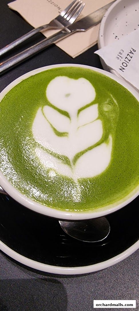 A close-up of a matcha latte with intricate foam art, served with cutlery.