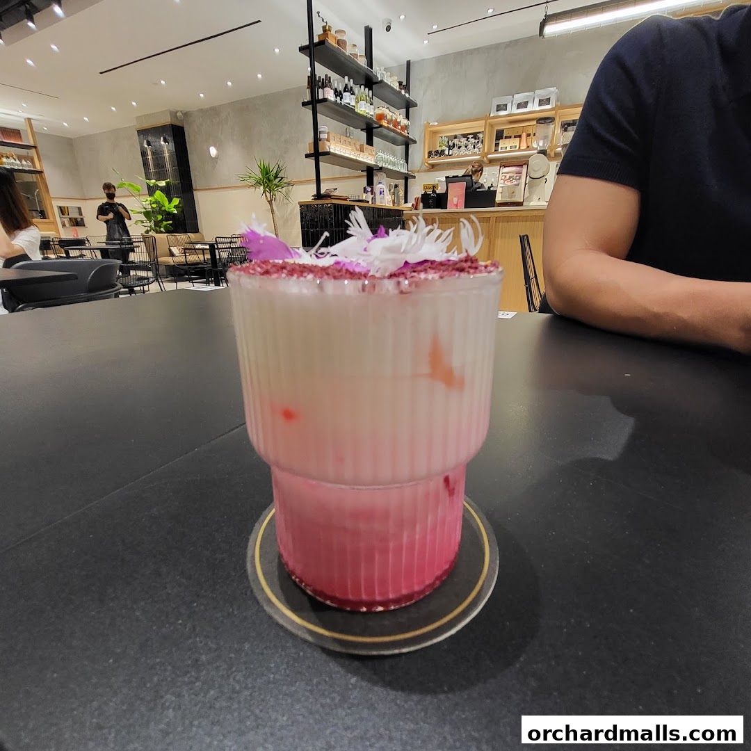 A beautifully garnished pink and white layered drink sits on a table in a cafe.