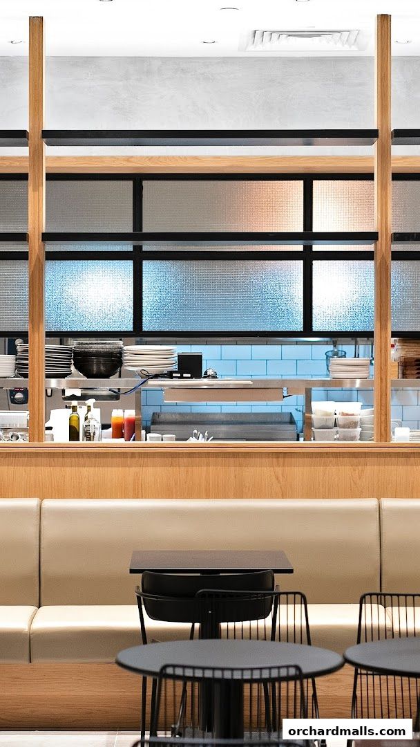 Interior view of a modern cafe with wooden accents, seating, and a visible kitchen counter.