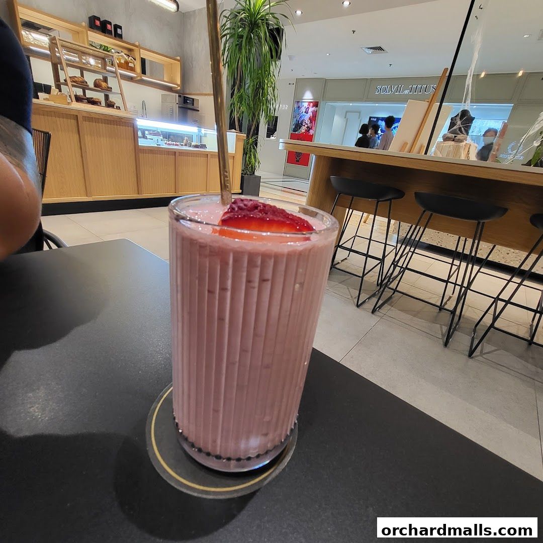 A refreshing pink smoothie with strawberry garnish sits on a table in a cafe.