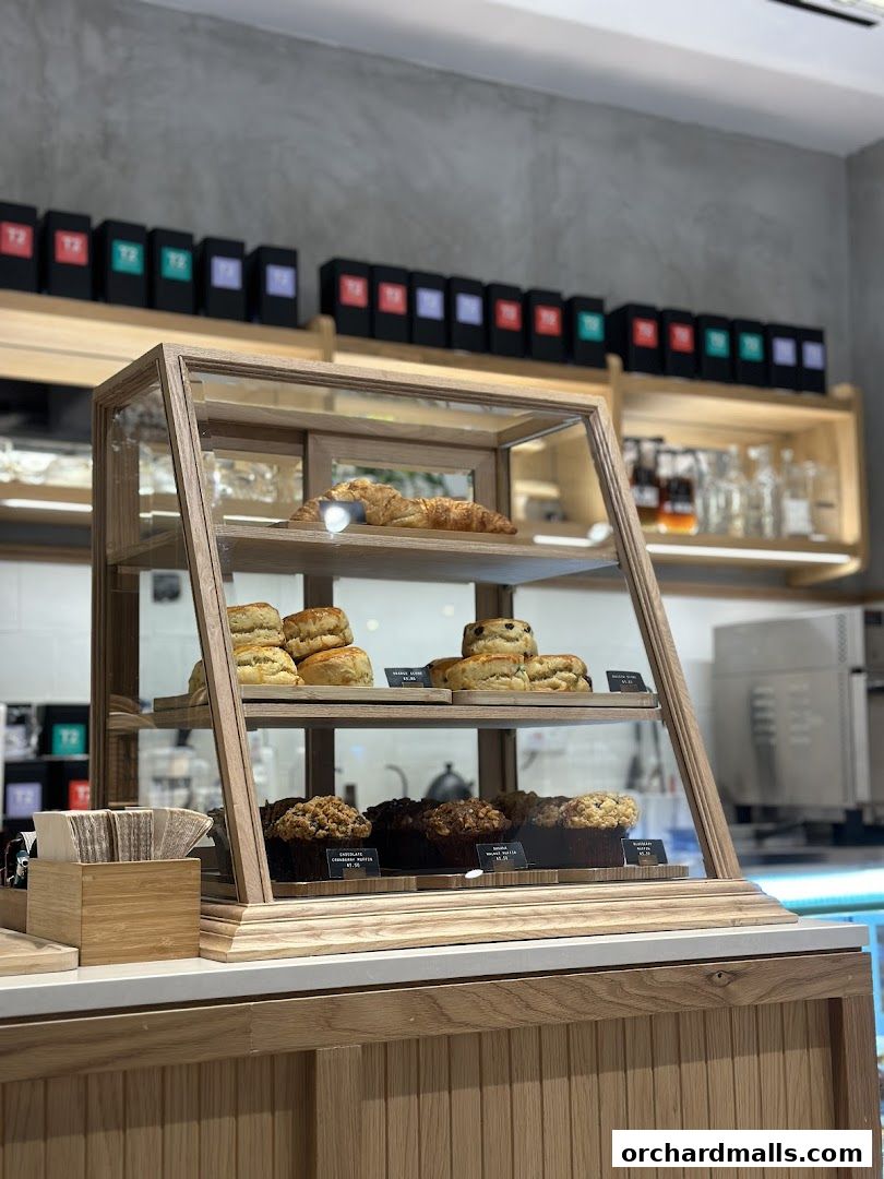 A display case filled with pastries and muffins, with tea boxes on a shelf above.