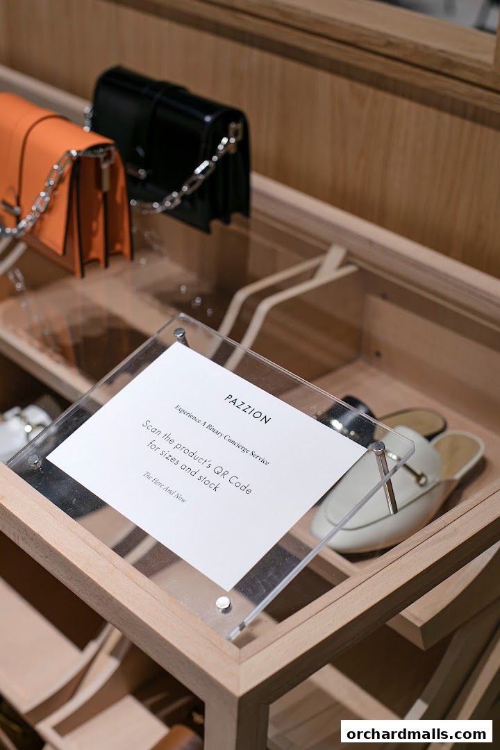 PAZZION store display featuring handbags and shoes with a QR code for concierge service.