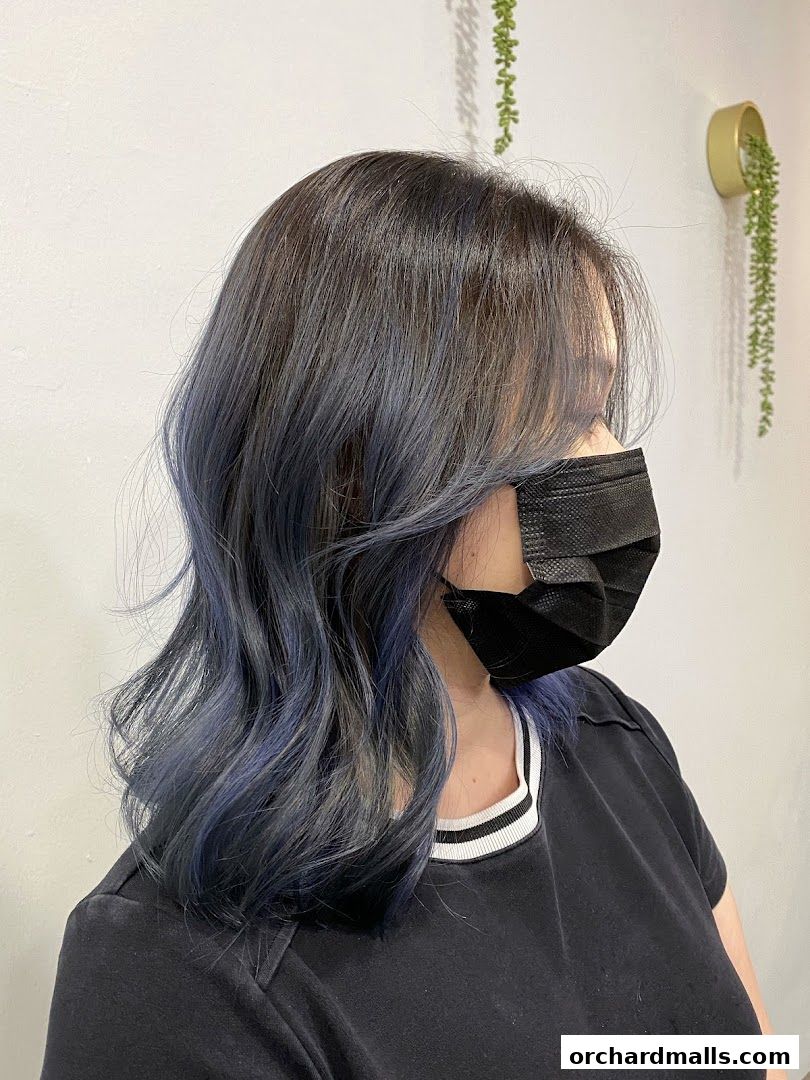 A woman with dark hair styled with blue highlights and a black face mask.