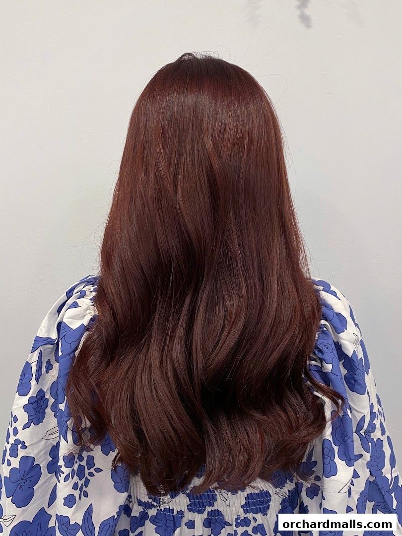 A person with long, wavy, dark reddish-brown hair styled with soft curls.