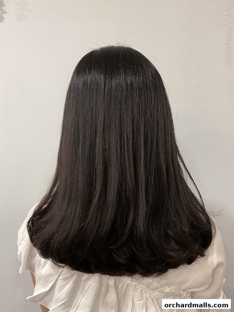 A person's back with long, dark, shiny, and healthy hair.
