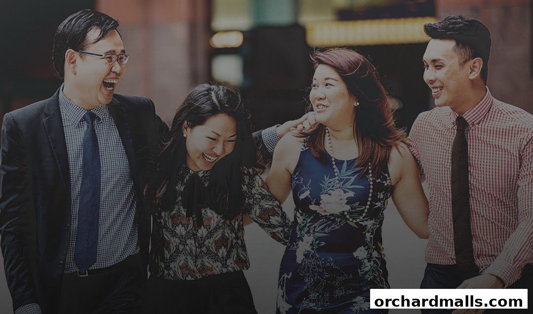 Four smiling people in business casual attire walking together outdoors.