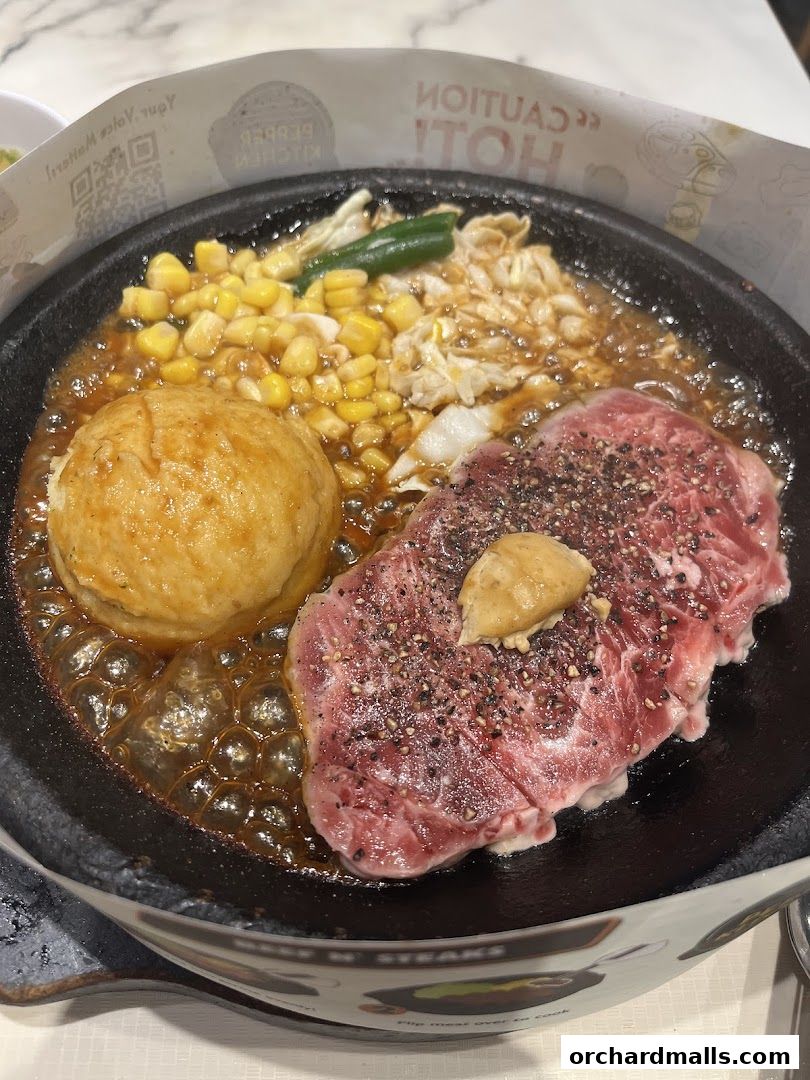 A sizzling steak served on a hot plate with corn, vegetables, and a side.