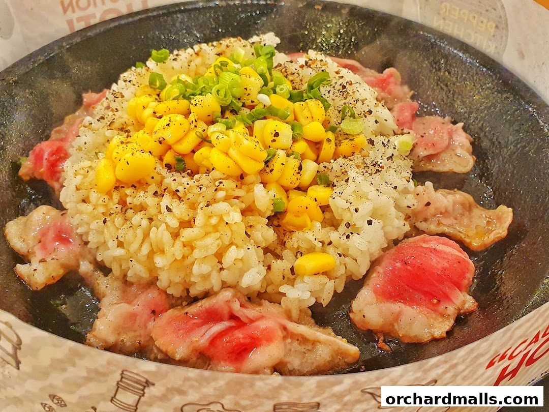 A sizzling hot plate of rice with beef and corn, garnished with spring onions.