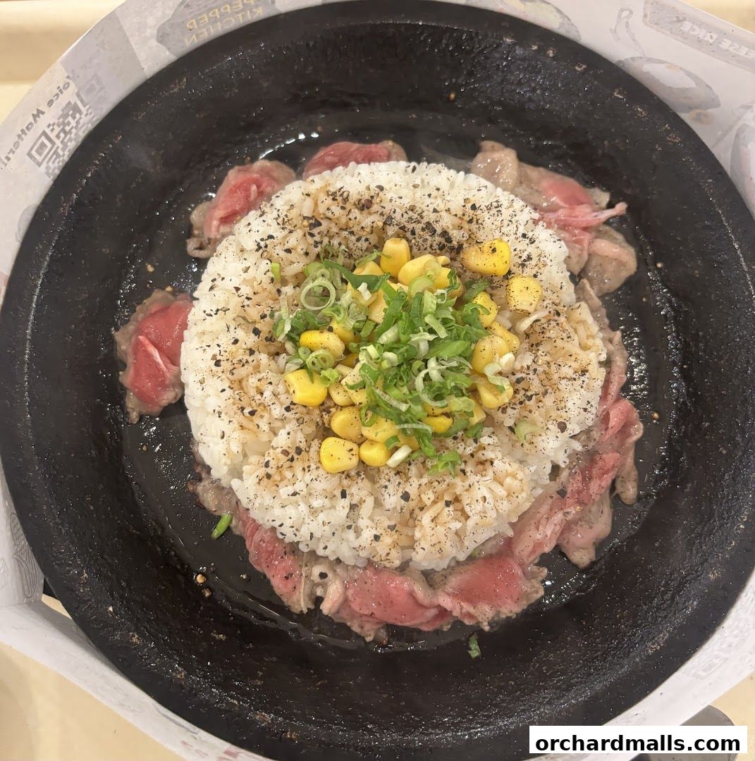 A sizzling hot plate dish with rice, thinly sliced beef, corn, and chopped scallions.