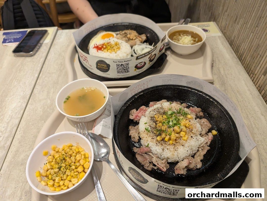 Two sizzling hot plates of rice with meat and corn, served with soup and corn.