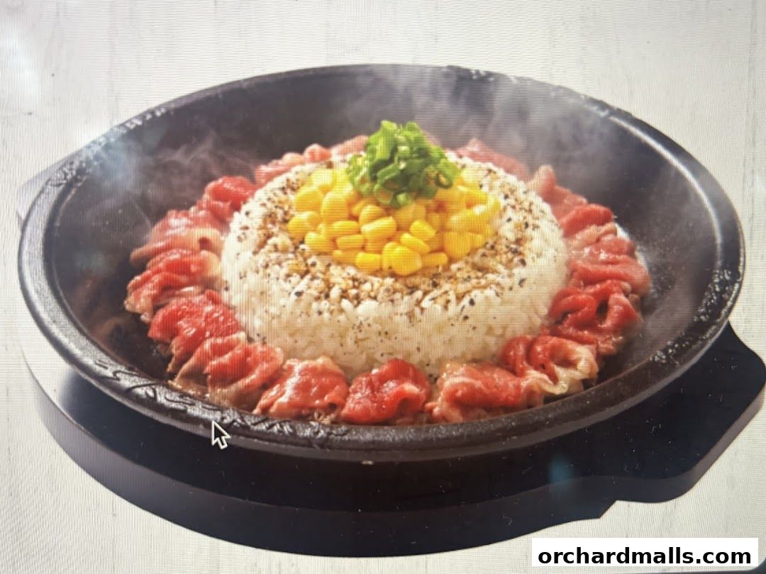 A sizzling hot plate of rice topped with corn and surrounded by thinly sliced beef.