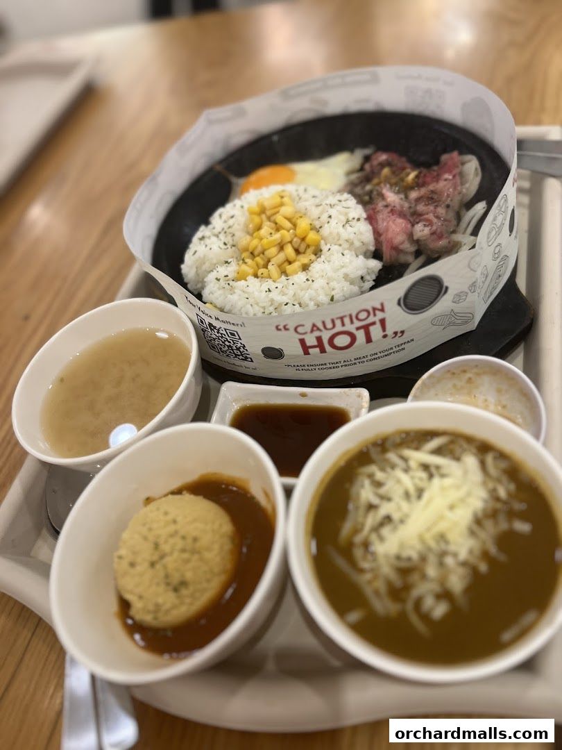 A sizzling hot plate meal with rice, corn, egg, and meat, served with soup and side dishes.