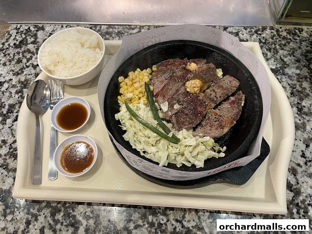 A sizzling steak dish served with rice, corn, and dipping sauces on a tray.