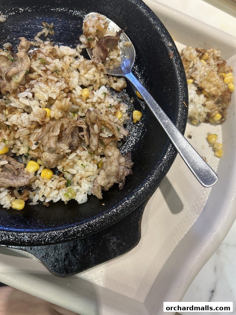 A close-up of a sizzling plate of beef fried rice with corn and a spoon.