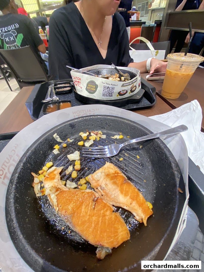 A close-up of a sizzling salmon dish with corn and onions, served with a drink.