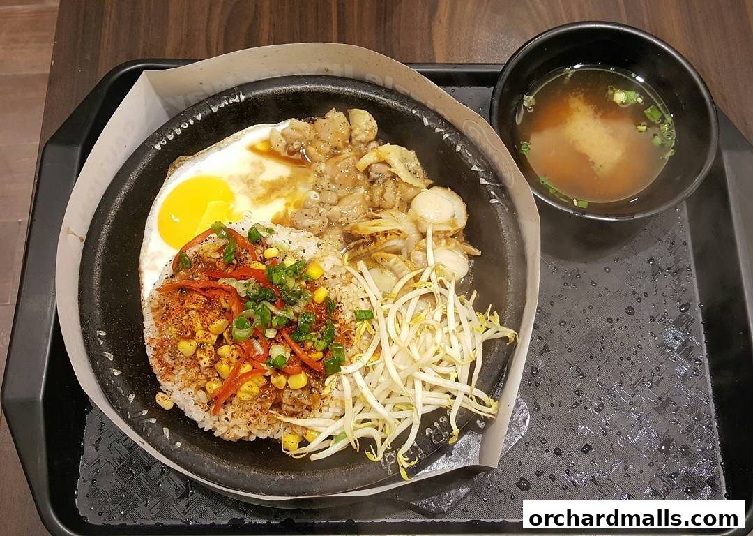 A sizzling hot plate of rice with a fried egg, scallops, chicken, and vegetables, served with miso soup.