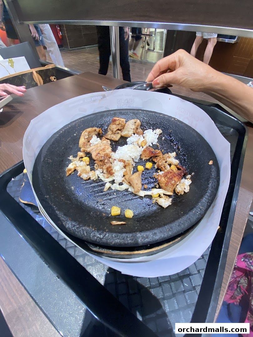 A close-up of a sizzling hot plate with grilled chicken, rice, and corn.