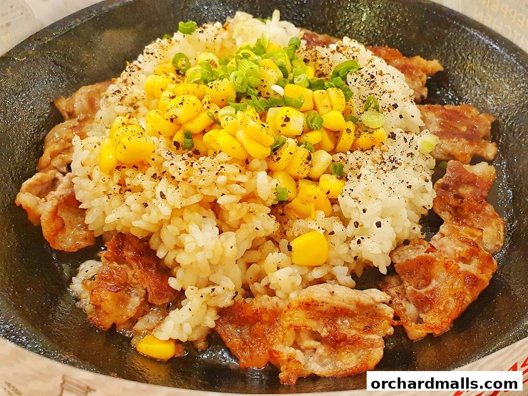 A sizzling hot plate of rice with corn, meat, and green onions.
