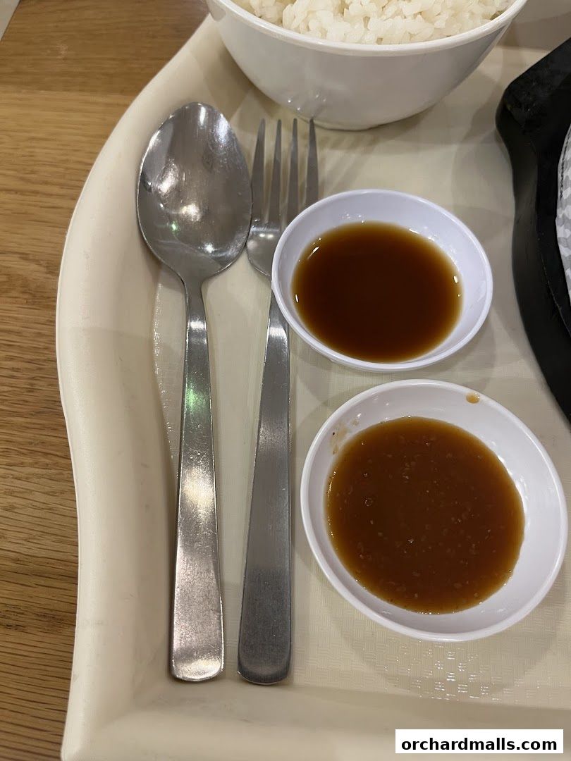 A close-up of a meal with rice, cutlery, and two dipping sauces on a tray.