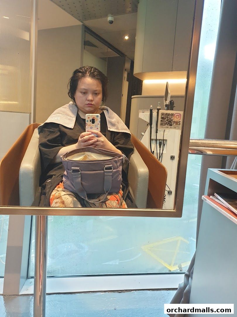 A woman sits in a salon chair, taking a selfie in the mirror.