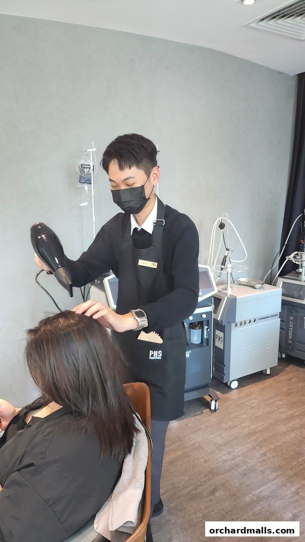 A stylist uses a hairdryer on a client's hair in a modern salon setting.