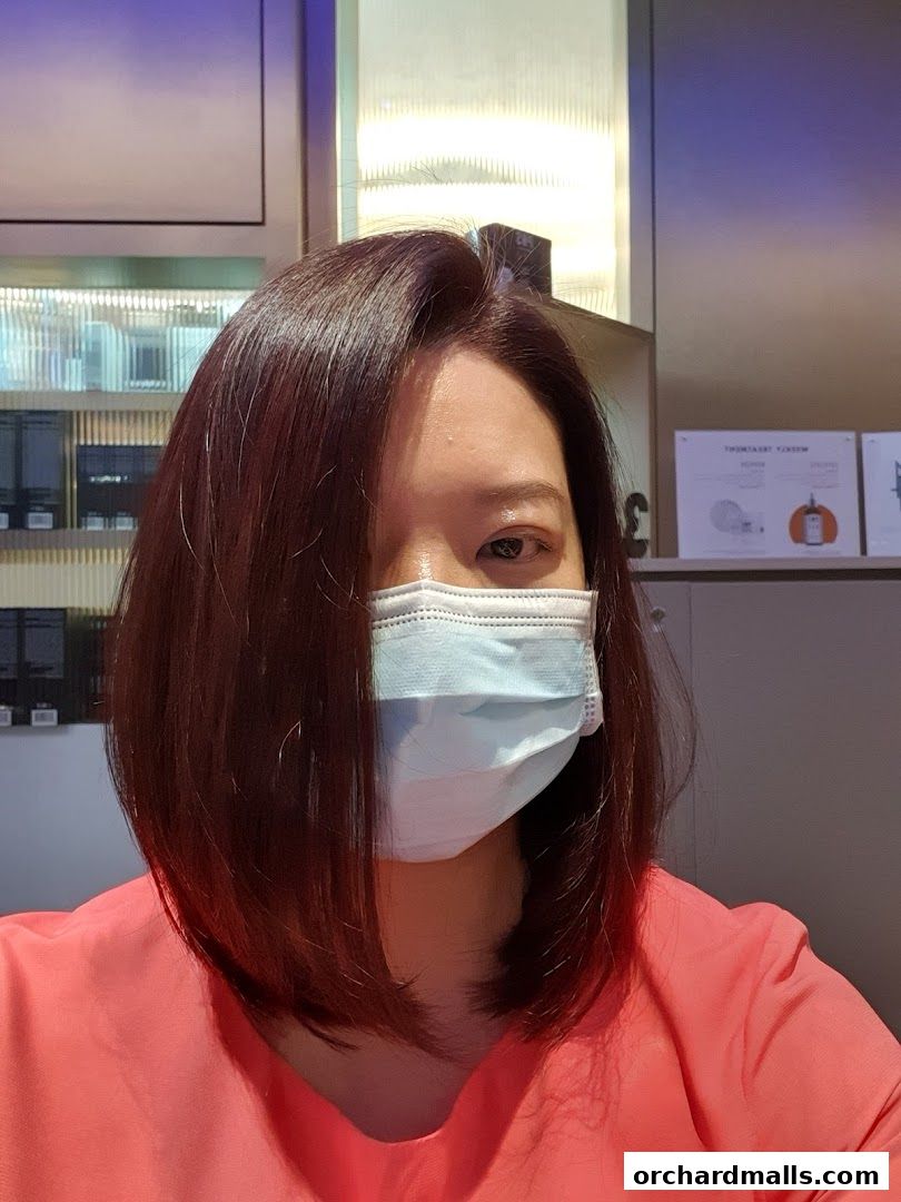 A woman with a mask and a bob haircut poses in front of a salon.