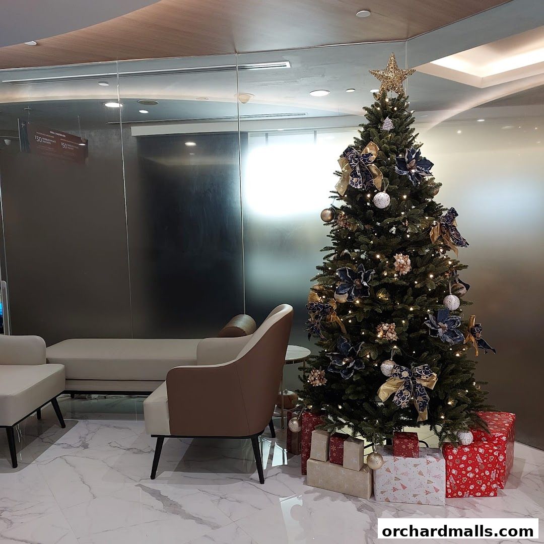A decorated Christmas tree with gifts sits in a modern waiting area with sofas.