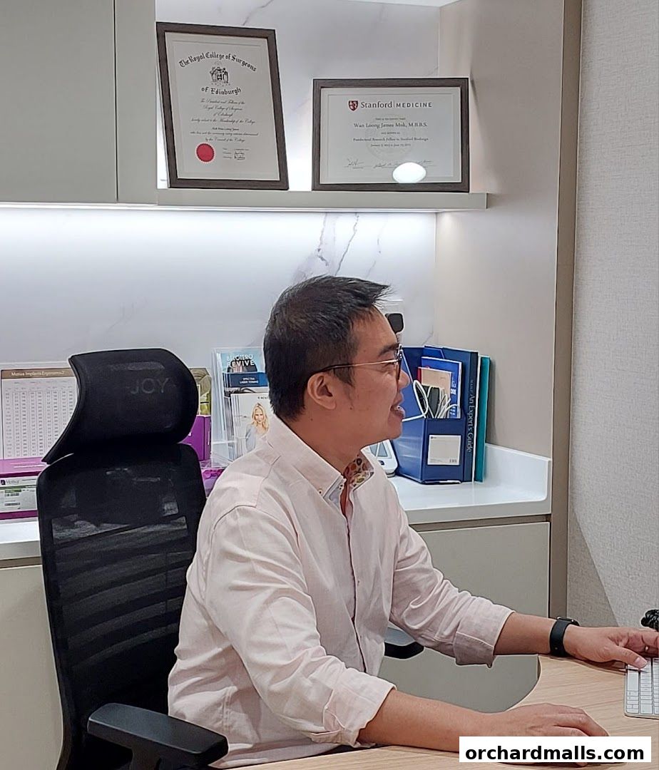 A doctor sits at a desk in an office, with medical certificates on the wall.