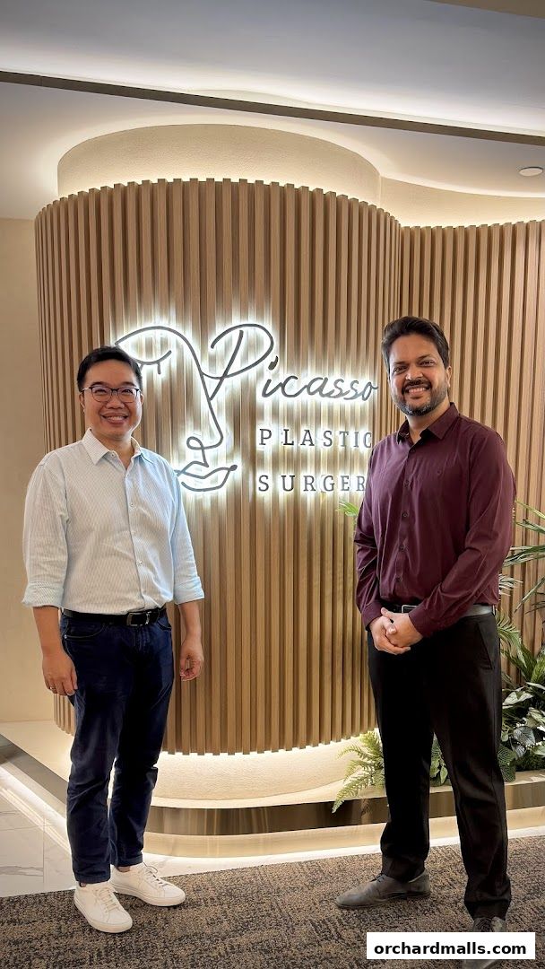 Two men stand in front of the Picasso Plastic Surgery logo at Wheelock Place.
