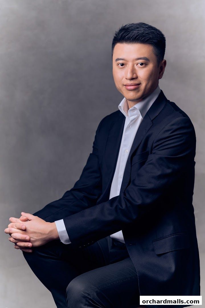 A man in a dark suit and white shirt poses against a grey backdrop.