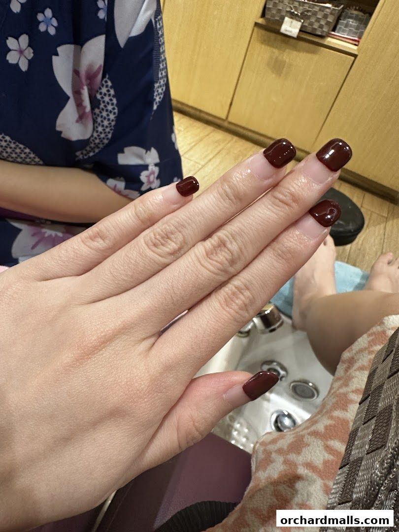 Close-up of a person's hands with freshly painted dark red nails at a nail spa.