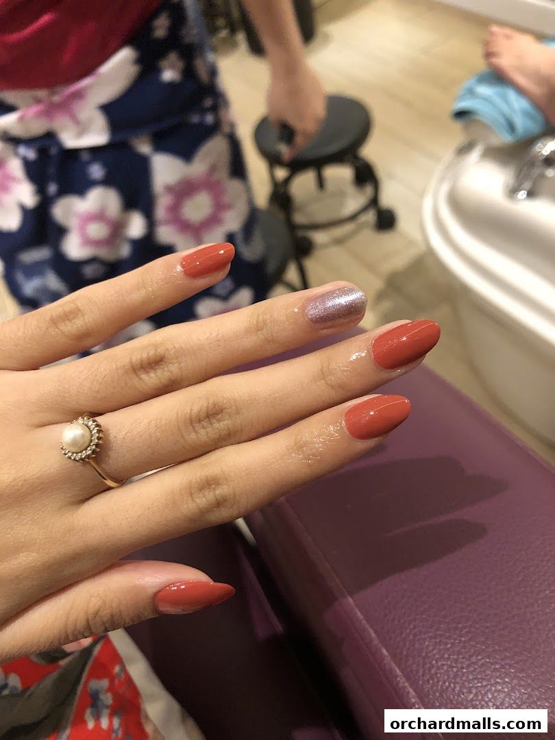 A close-up of a woman's hands with freshly painted nails in a reddish-orange hue.