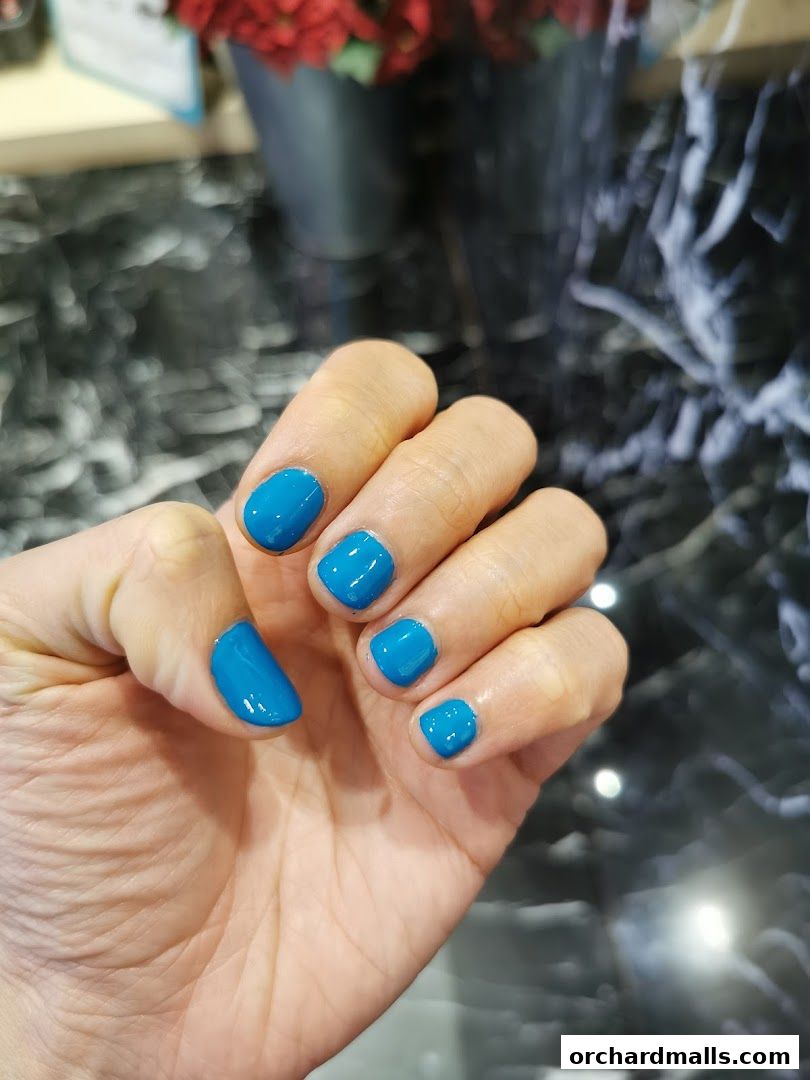 A hand with bright blue gel nails is displayed against a marbled background.