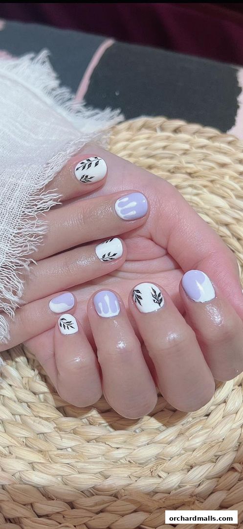 Close-up of hands with a delicate white and lavender nail art design featuring leaf motifs.