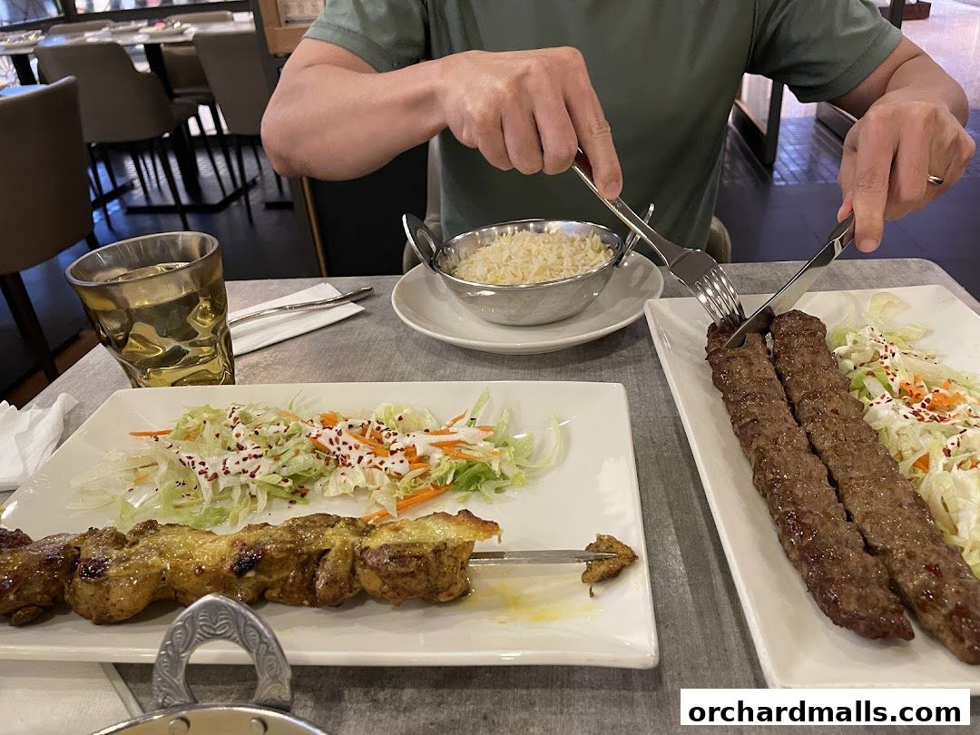 A person is eating grilled meat skewers and rice at a restaurant.