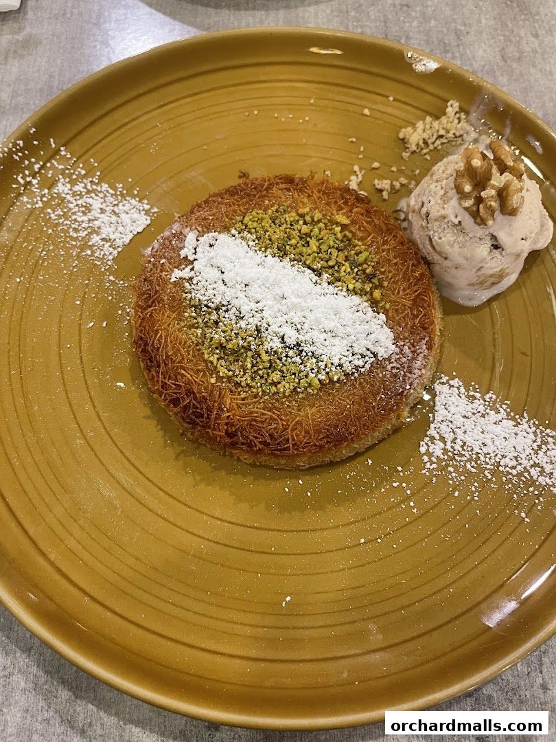 A delicious kunafa dessert with ice cream and nuts on a golden plate.