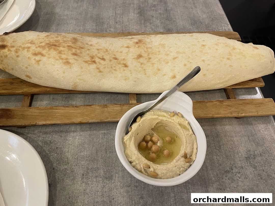 A close-up of hummus with pine nuts and a large piece of flatbread on a wooden board.