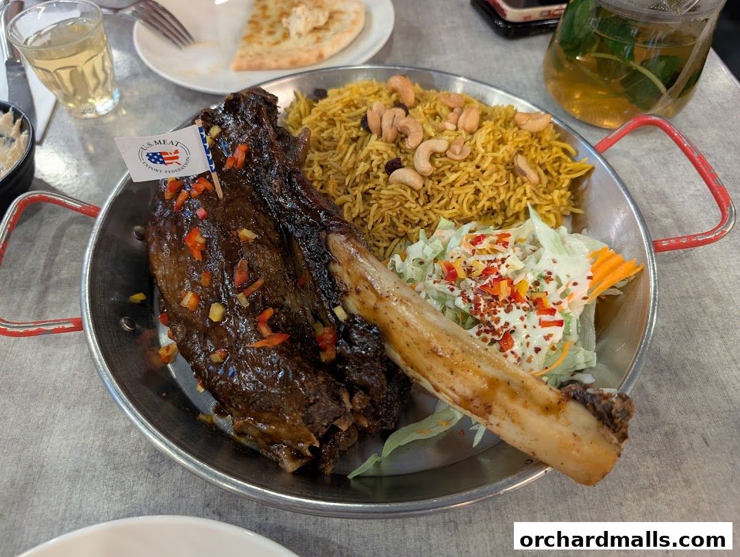 A plate of lamb shank with rice, salad, and a side of naan bread and drink.