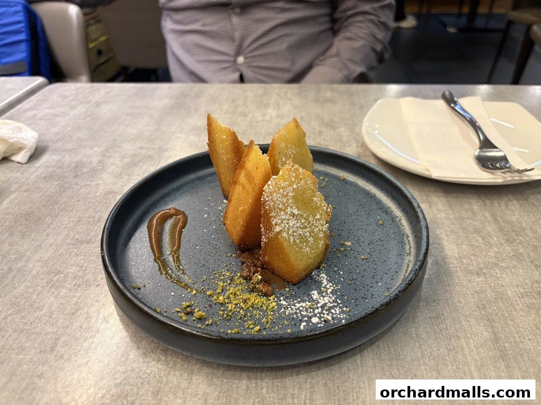A plate of fried pastries dusted with powdered sugar and pistachios, served with sauce.