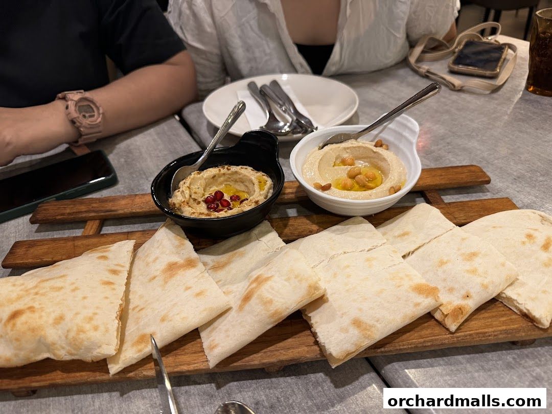 Two bowls of hummus with pita bread served on a wooden platter.