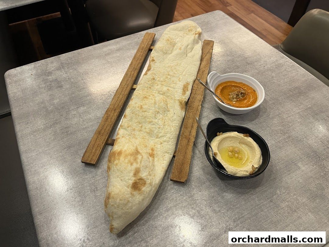 Flatbread served with hummus and a red pepper dip on a table.