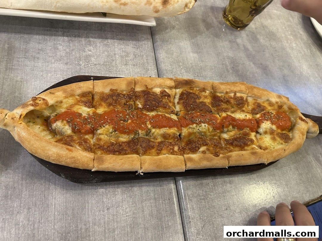 A delicious-looking Turkish pide with cheese and tomato sauce on a wooden board.